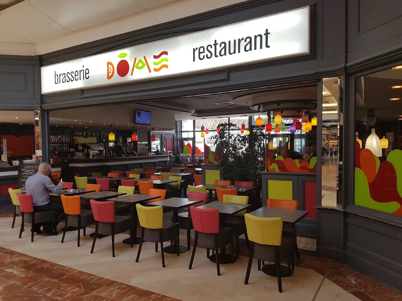 La salle de la brasserie Le Dôme : tables et chaises colorées, bar et enseigne
